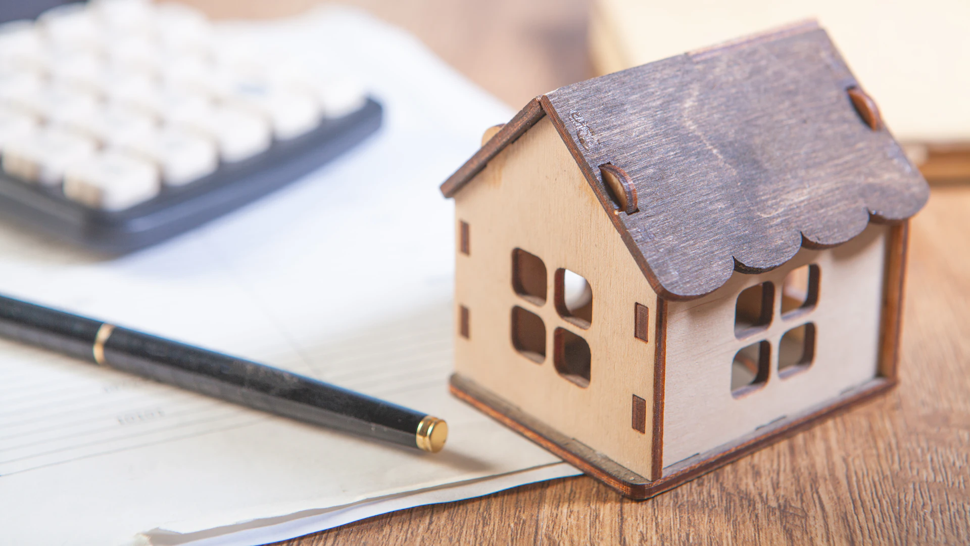 Wooden house model beside a calculator, sale paperwork and a pen, used to explain a Houston seller's estimated net proceeds / 木质房屋模型、计算器、交易文件与笔,用于说明休斯顿卖家的预计净到手金额